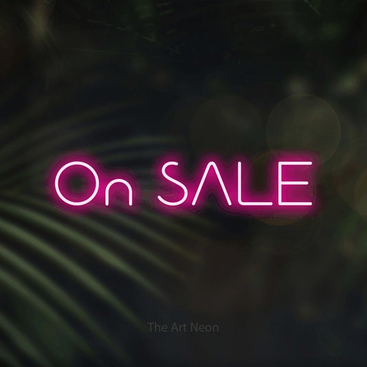 Hot pink LED neon sign reading "On Sale" against dark blurred palm leaves