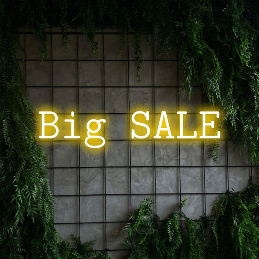 Yellow LED neon sign reading "Big Sale" against a green grid wall with foliage