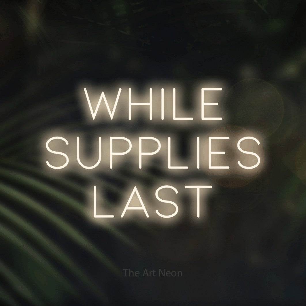 Warm white LED neon sign reading "While Supplies Last" against dark blurred palm leaves