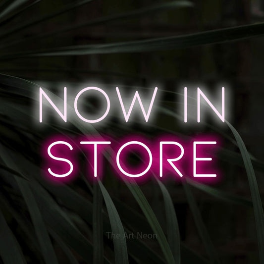 Hot pink and cool white LED neon sign reading "Now in Store" against dark tropical leaves