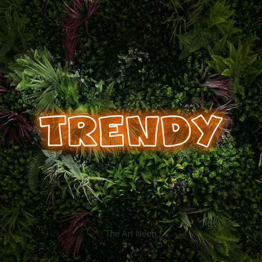 Orange outline-style LED neon sign reading "Trendy" against a lush garden wall with pink flowers