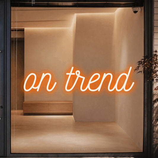 Orange script-style LED neon sign reading "On Trend" against a warm beige alcove wall