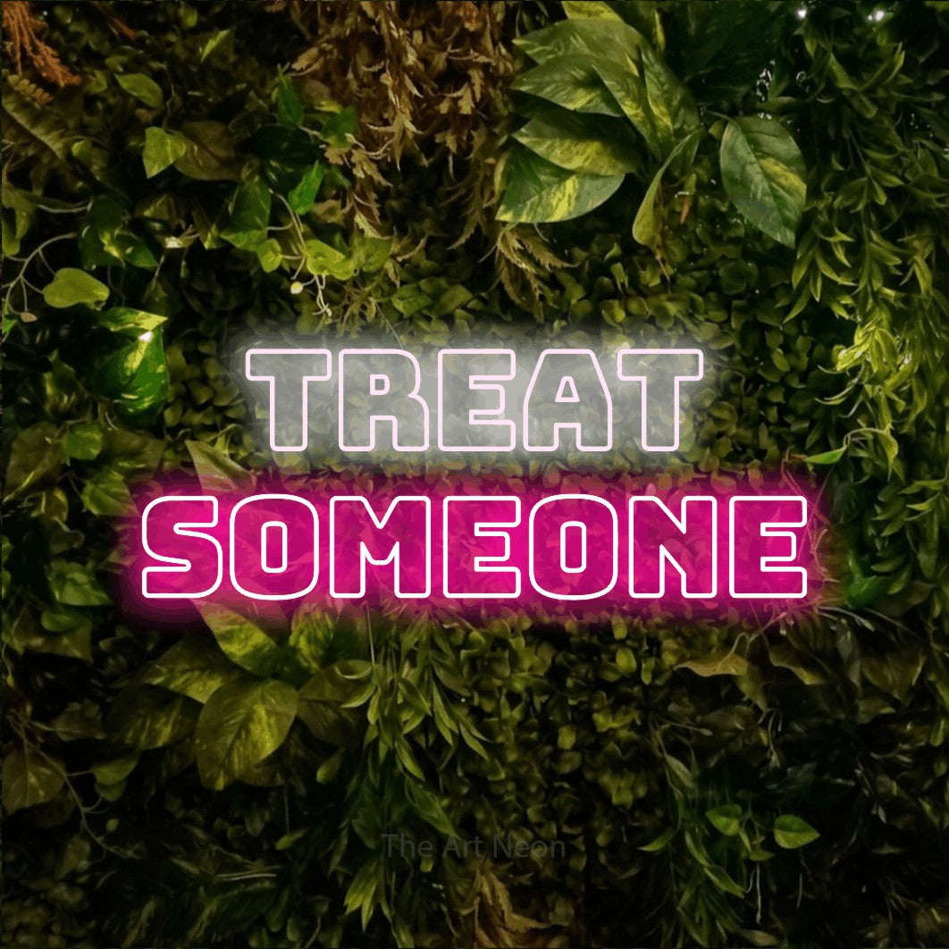 Hot pink and cool white outline-style LED neon sign reading "Treat Someone" against a textured moss and foliage wall