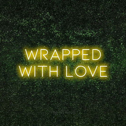 Yellow LED neon sign reading "Wrapped with Love" against a textured green moss wall