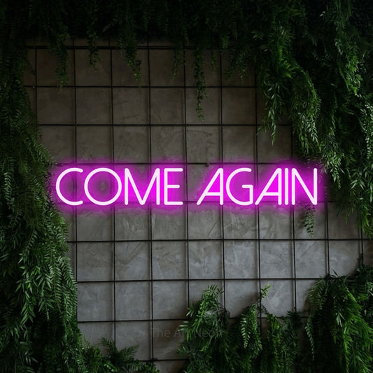 Pink LED neon sign reading "Come Again" against a green grid wall with foliage