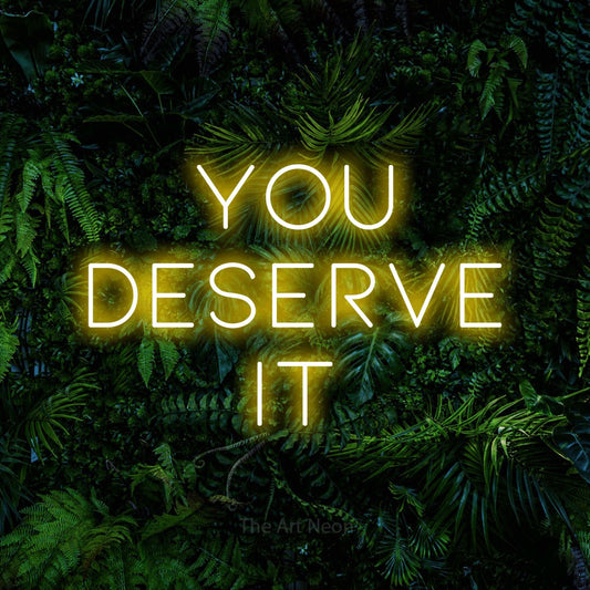 Yellow LED neon sign reading "You Deserve It" against a dense tropical foliage wall