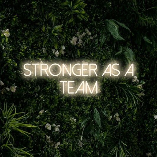 Warm white LED neon sign reading "Stronger as a Team" against a leafy green wall for office décor