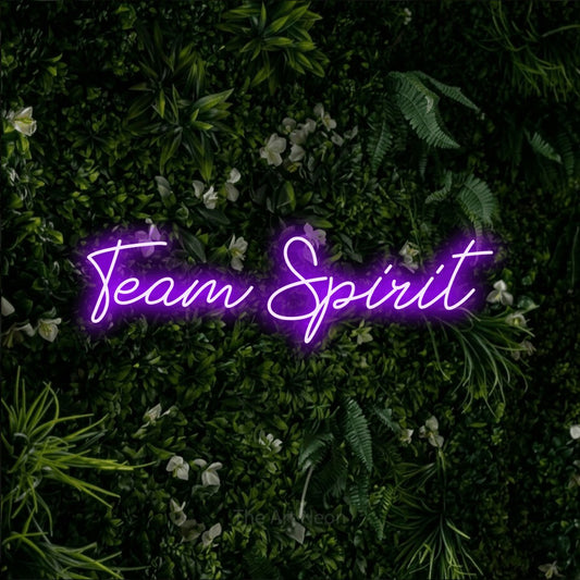 Purple script-style LED neon sign reading "Team Spirit" against a leafy green wall for office décor
