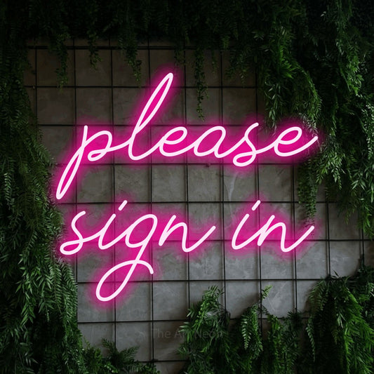 Hot pink script-style LED neon sign reading "Please Sign In" against a green grid wall with foliage for office décor