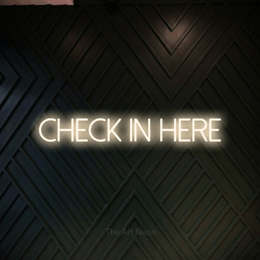 Warm white LED neon sign reading "Check In Here" against a dark geometric wood wall for office décor