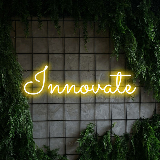 Yellow LED neon sign reading "Innovate" against a green grid wall with foliage for office décor