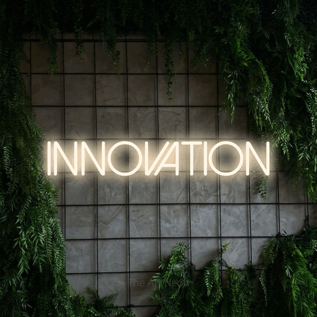 Warm white LED neon sign reading "Innovation" against a green grid wall with foliage for office décor