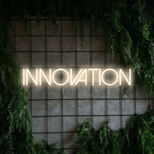 Warm white LED neon sign reading "Innovation" against a green grid wall with foliage for office décor
