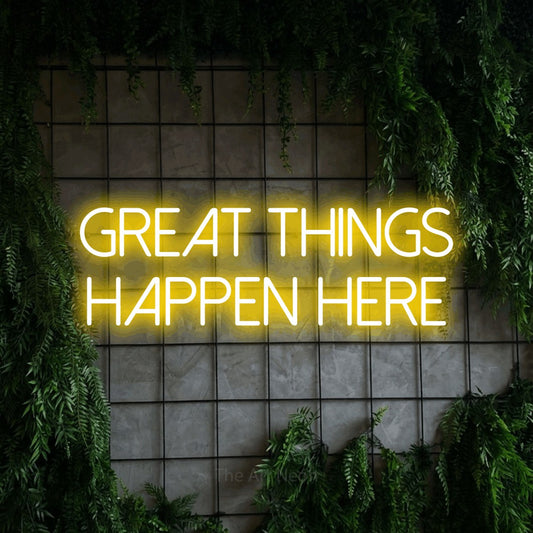 Yellow LED neon sign reading "Great Things Happen Here" against a green grid wall with foliage for office décor