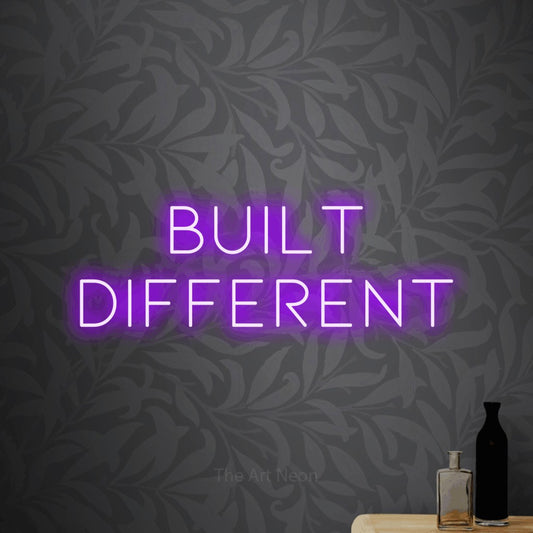 Purple LED neon sign reading "Built Different" against light grey floral wallpaper for office décor