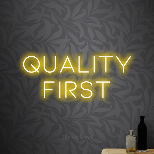 Yellow LED neon sign reading "Quality First" against light grey floral wallpaper for office décor