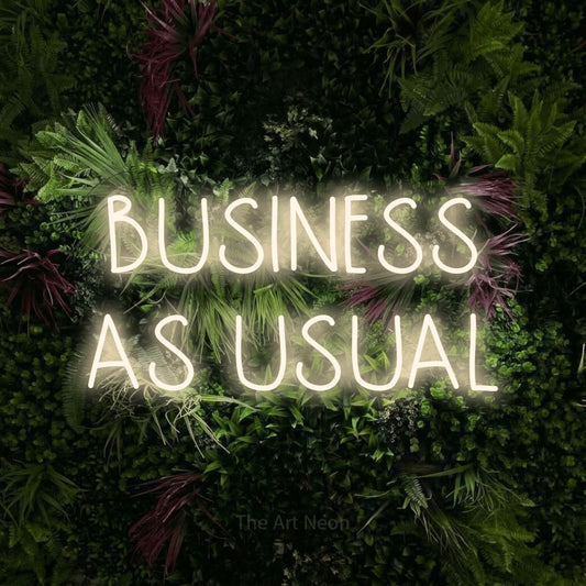 Enseigne néon à DEL à lumière blanche chaude, affichant « Business as Usual » sur un mur de jardin luxuriant aux fleurs roses, pour décorer un bureau