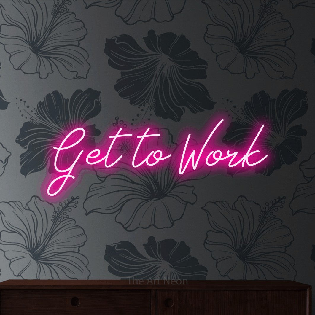Hot pink script-style LED neon sign reading "Get to Work" against grey floral wallpaper for office décor