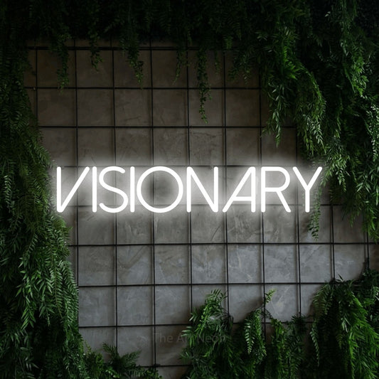 Cool white LED neon sign reading "Visionary" against a green grid wall with foliage for office décor