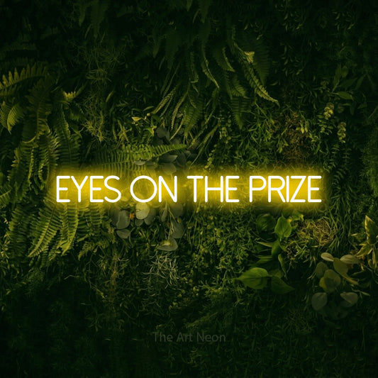 Yellow LED neon sign reading "Eyes on the Prize" against a moss-covered green wall for office décor