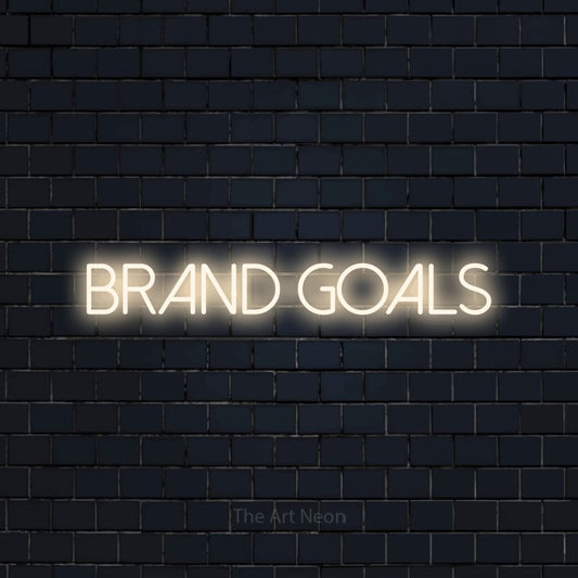 Warm white LED neon sign reading "Brand Goals" against a dark navy brick wall for office décor