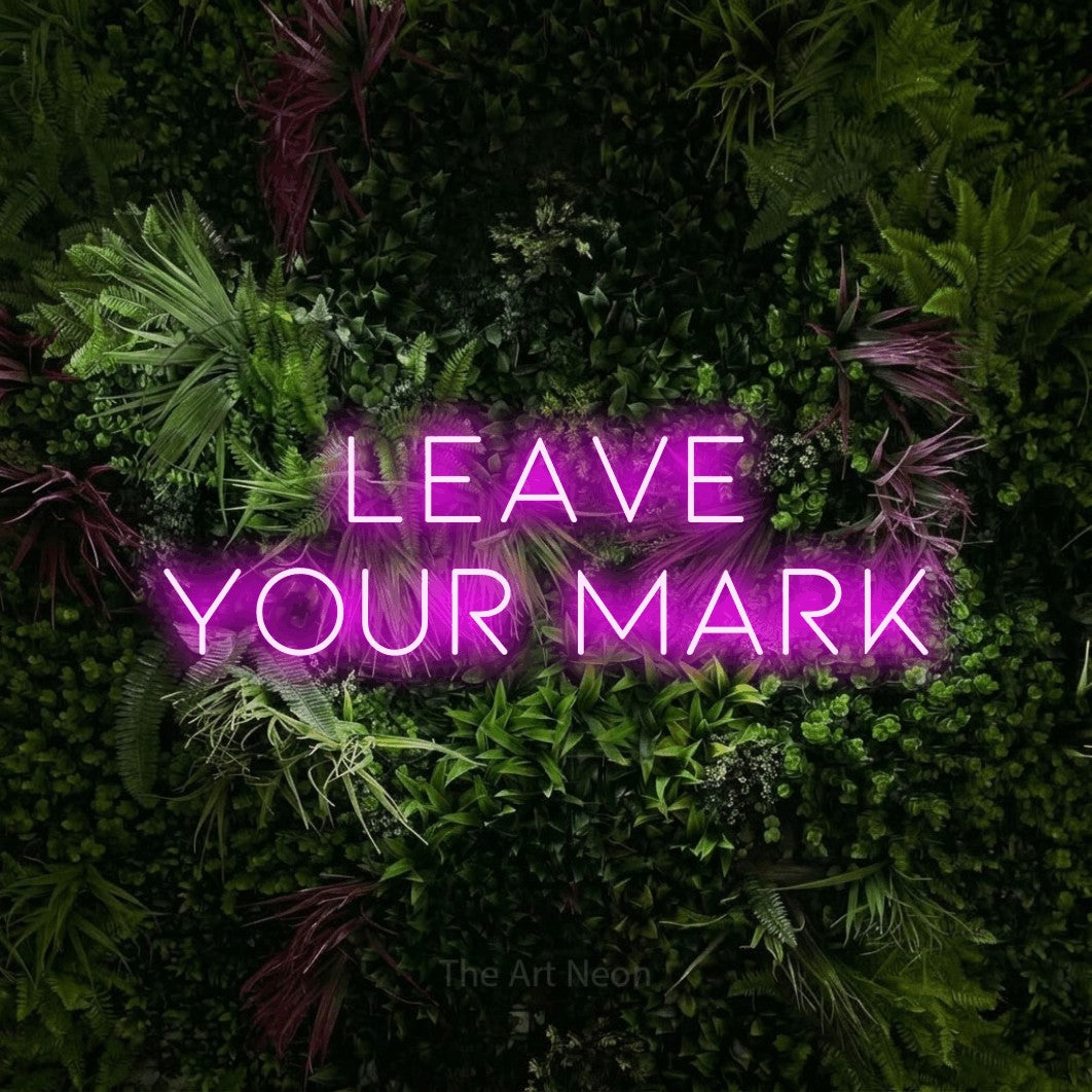 Pink LED neon sign reading "Leave Your Mark" against a lush garden wall with pink flowers for office décor