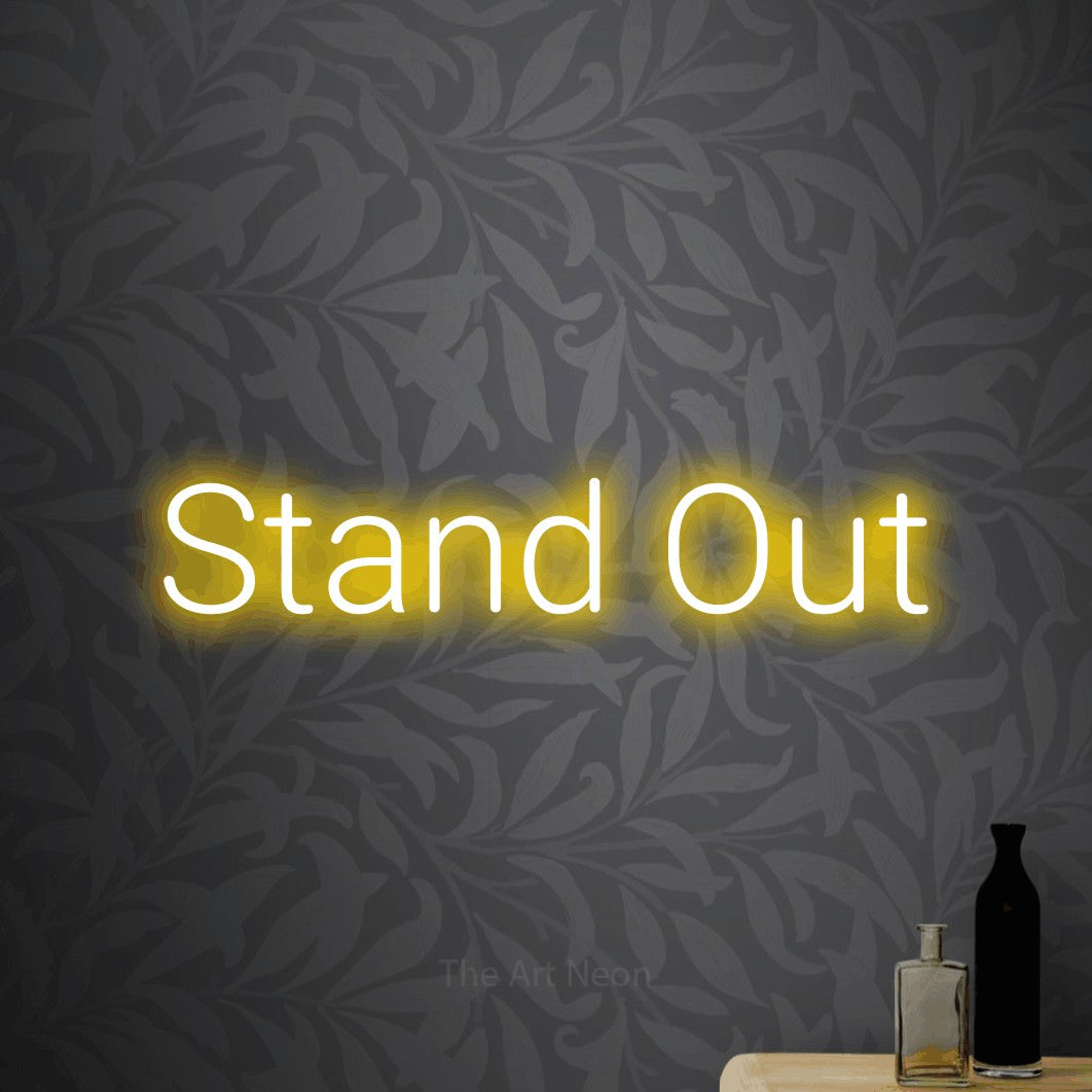Yellow LED neon sign reading "Stand Out" against light grey floral wallpaper for office décor