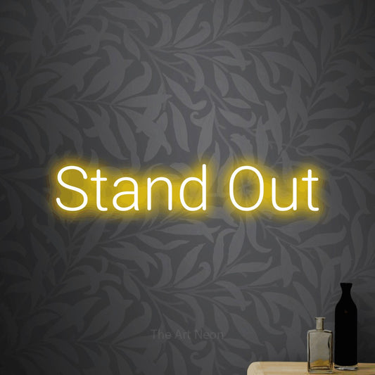 Yellow LED neon sign reading "Stand Out" against light grey floral wallpaper for office décor