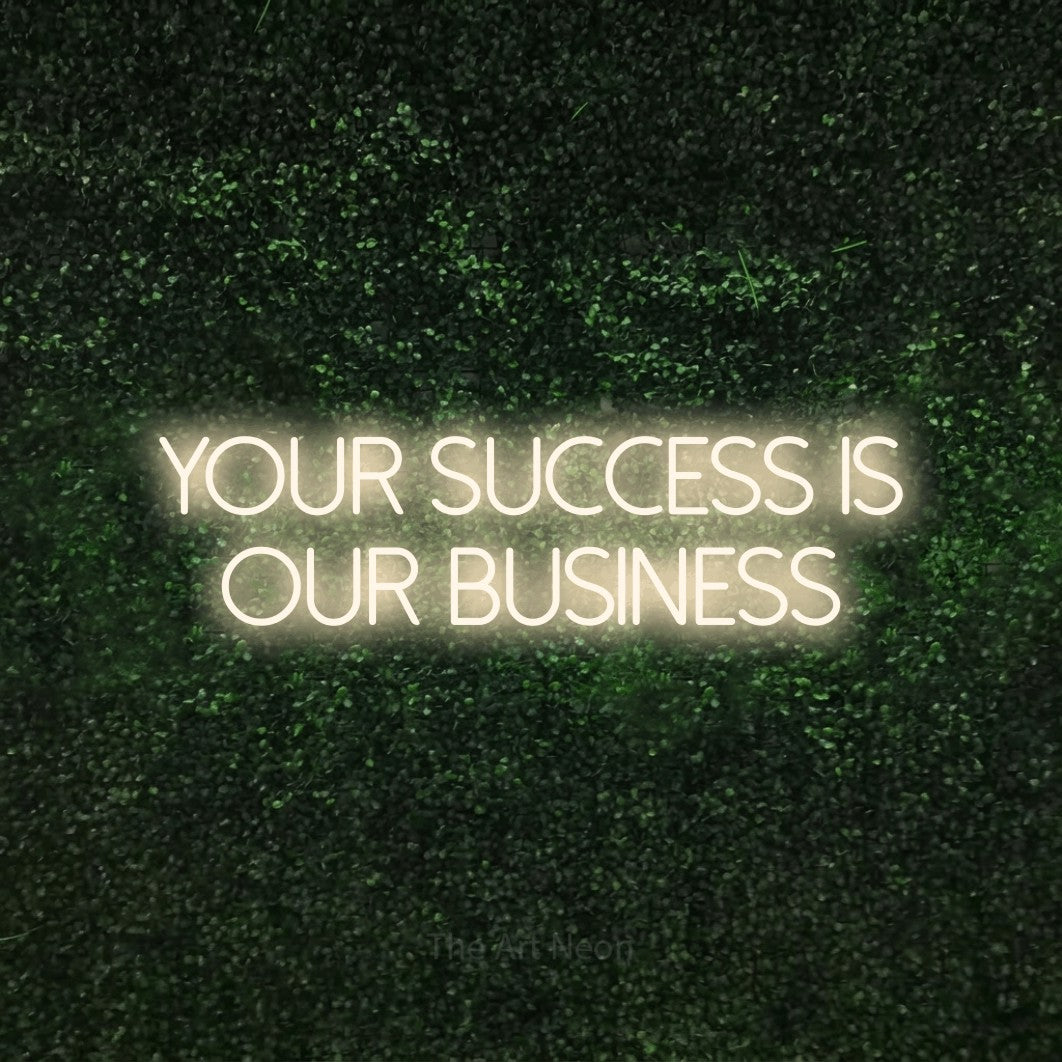 Warm white LED neon sign reading "Your Success is Our Business" against a textured green moss wall for office décor