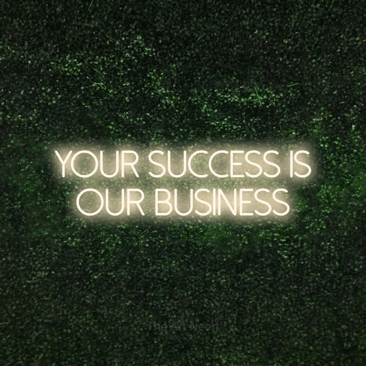 Warm white LED neon sign reading "Your Success is Our Business" against a textured green moss wall for office décor