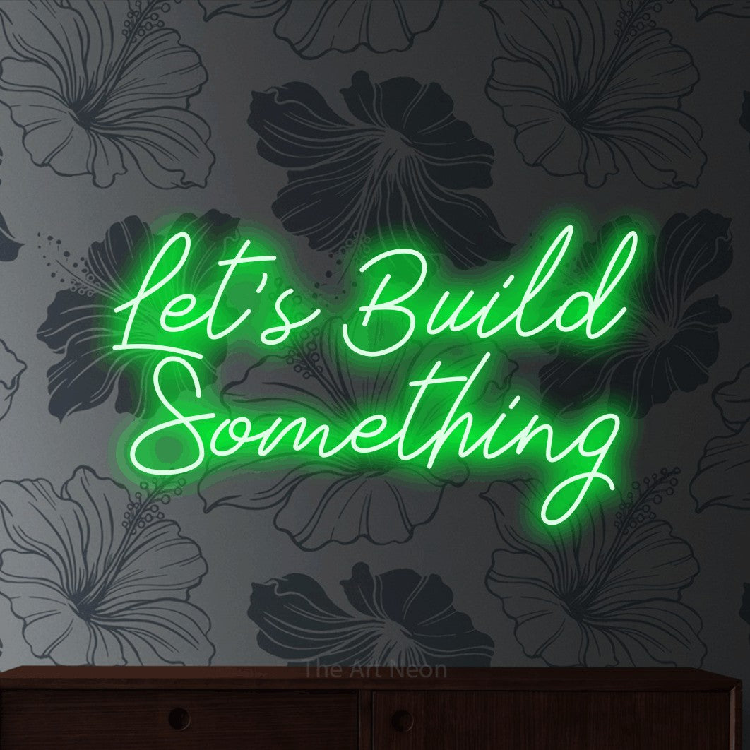 Green script-style LED neon sign reading "Let's Build Something" against grey floral wallpaper for office décor