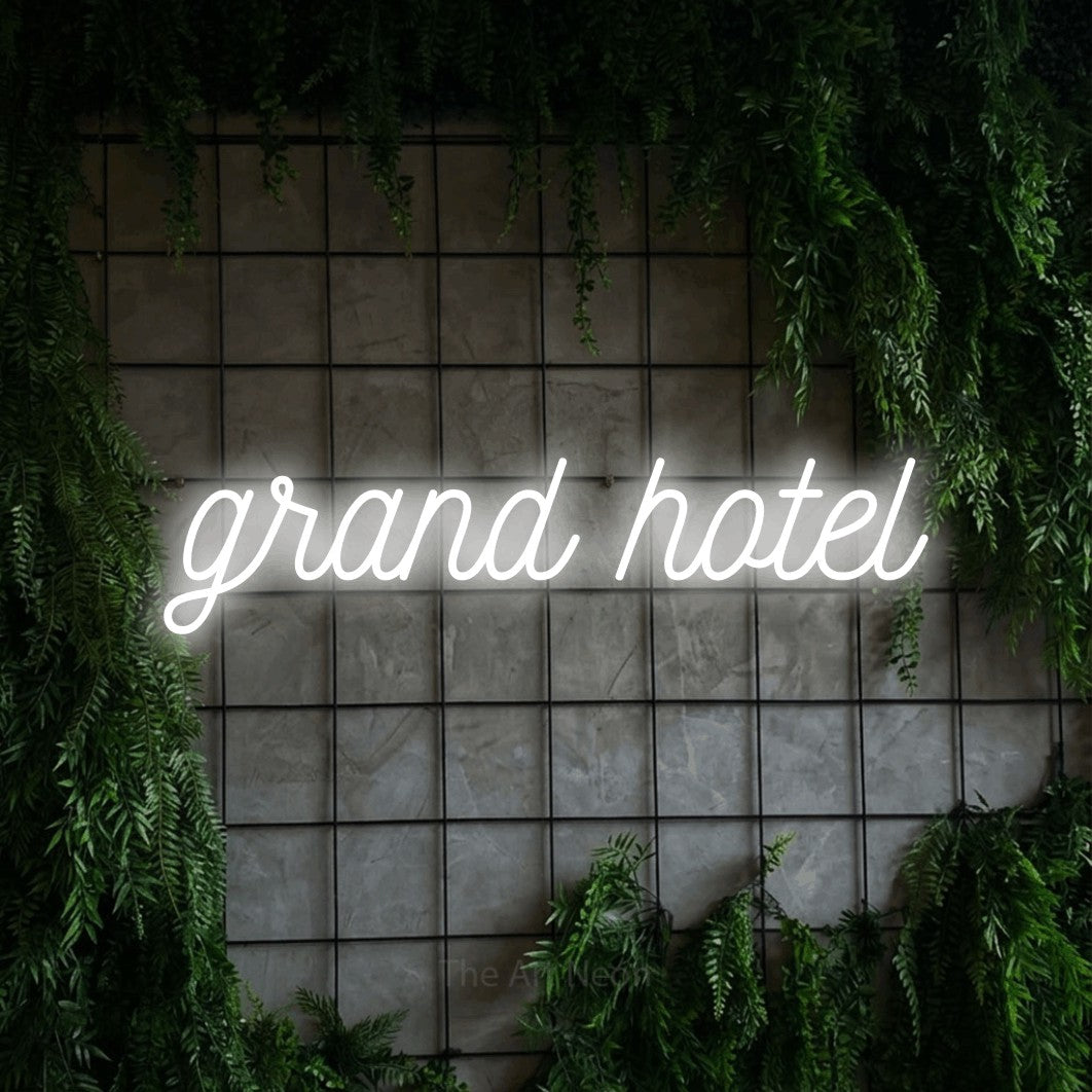 Cool white script-style LED neon sign reading "Grand Hotel" against a green grid wall with foliage for hotel décor