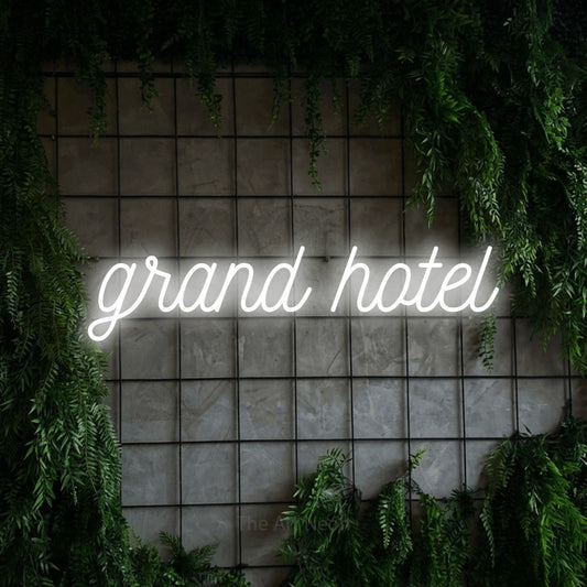 Cool white script-style LED neon sign reading "Grand Hotel" against a green grid wall with foliage for hotel décor