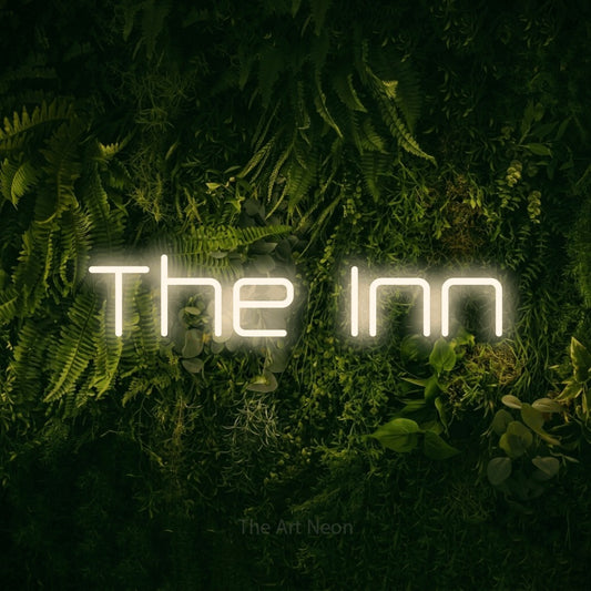 Warm white outline-style LED neon sign reading "The Inn" against a moss-covered green wall for hotel décor