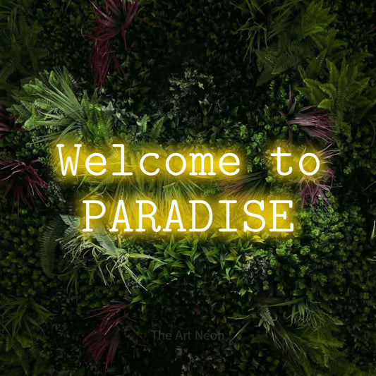 Yellow LED neon sign reading "Welcome to Paradise" against a lush garden wall with pink flowers for hotel décor