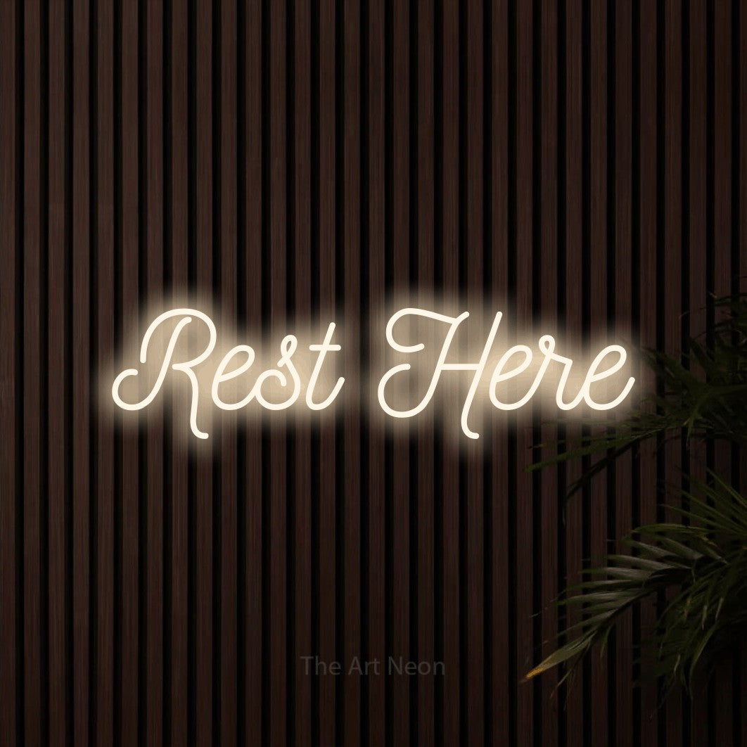 Warm white script-style LED neon sign reading "Rest Here" against dark wooden slats for hotel décor
