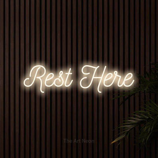 Warm white script-style LED neon sign reading "Rest Here" against dark wooden slats for hotel décor