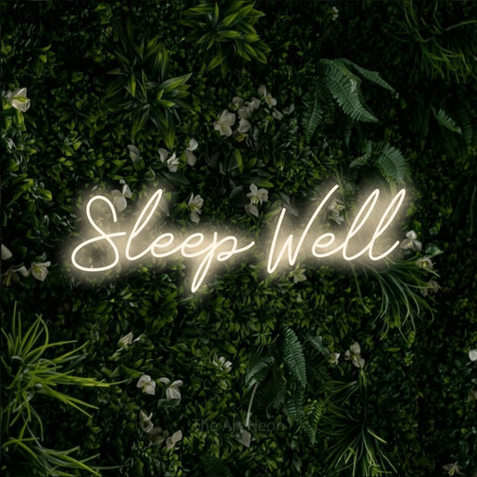 Warm white script-style LED neon sign reading "Sleep Well" against a leafy green wall for hotel décor