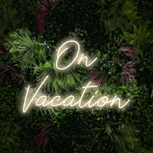 Warm white script-style LED neon sign reading "On Vacation" against a lush garden wall with pink flowers for hotel décor