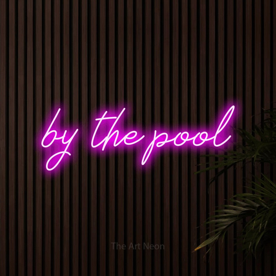 Pink script-style LED neon sign reading "By the Pool" against dark wooden slats for hotel décor