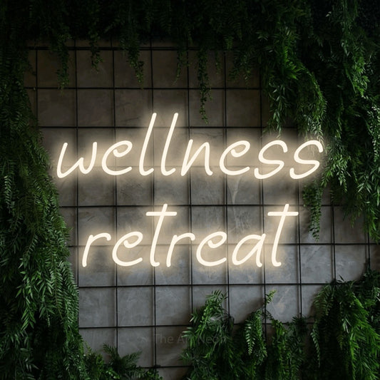 Warm white LED neon sign reading "Wellness Retreat" against a green grid wall with foliage for hotel décor