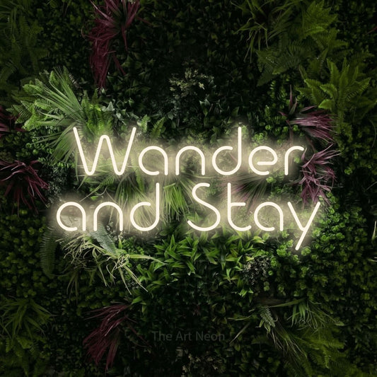 Warm white LED neon sign reading "Wander and Stay" against a lush garden wall with pink flowers for hotel décor