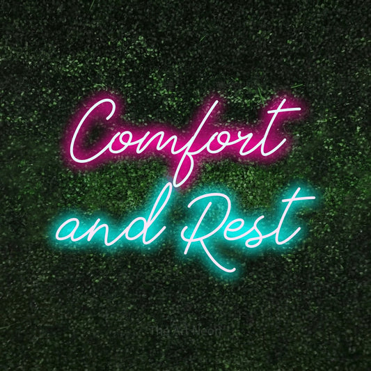 Ice blue and hot pink script-style LED neon sign reading "Comfort and Rest" against a textured green moss wall