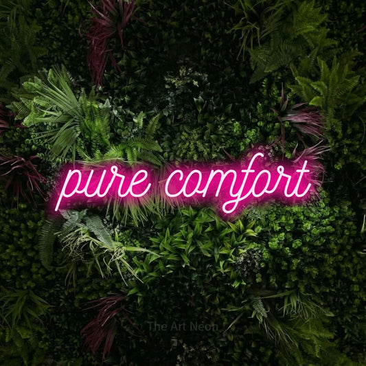 Hot pink script-style LED neon sign reading "Pure Comfort" against a lush garden wall with pink flowers for hotel décor