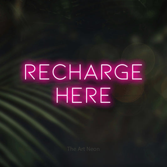 Hot pink LED neon sign reading "Recharge Here" against dark blurred palm leaves for hotel décor