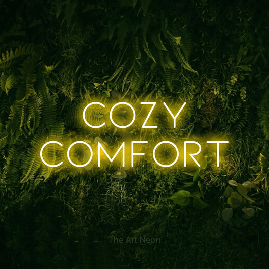 Yellow LED neon sign reading "Cozy Comfort" against a moss-covered green wall for hotel décor
