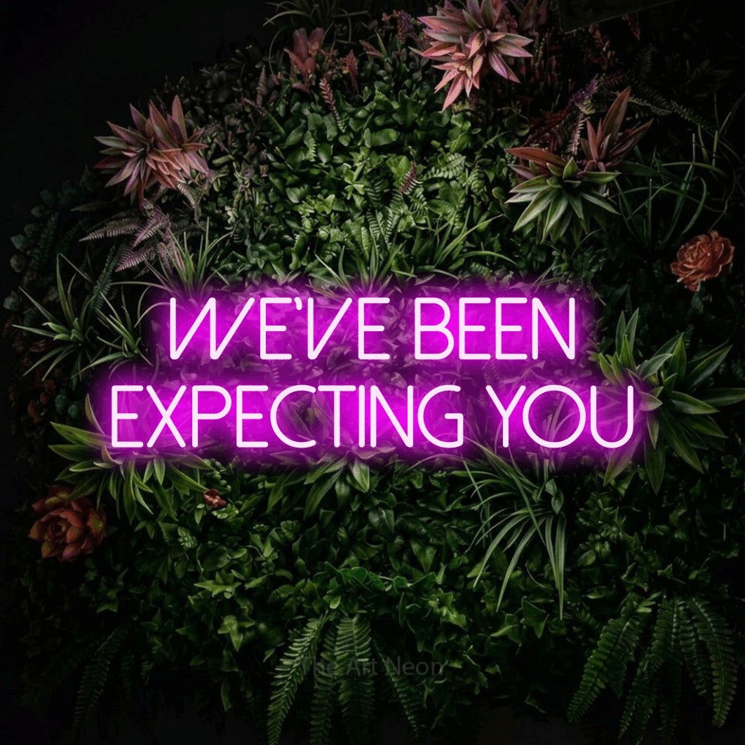 Pink LED neon sign reading "We've Been Expecting You" against a flowering garden wall for hotel décor