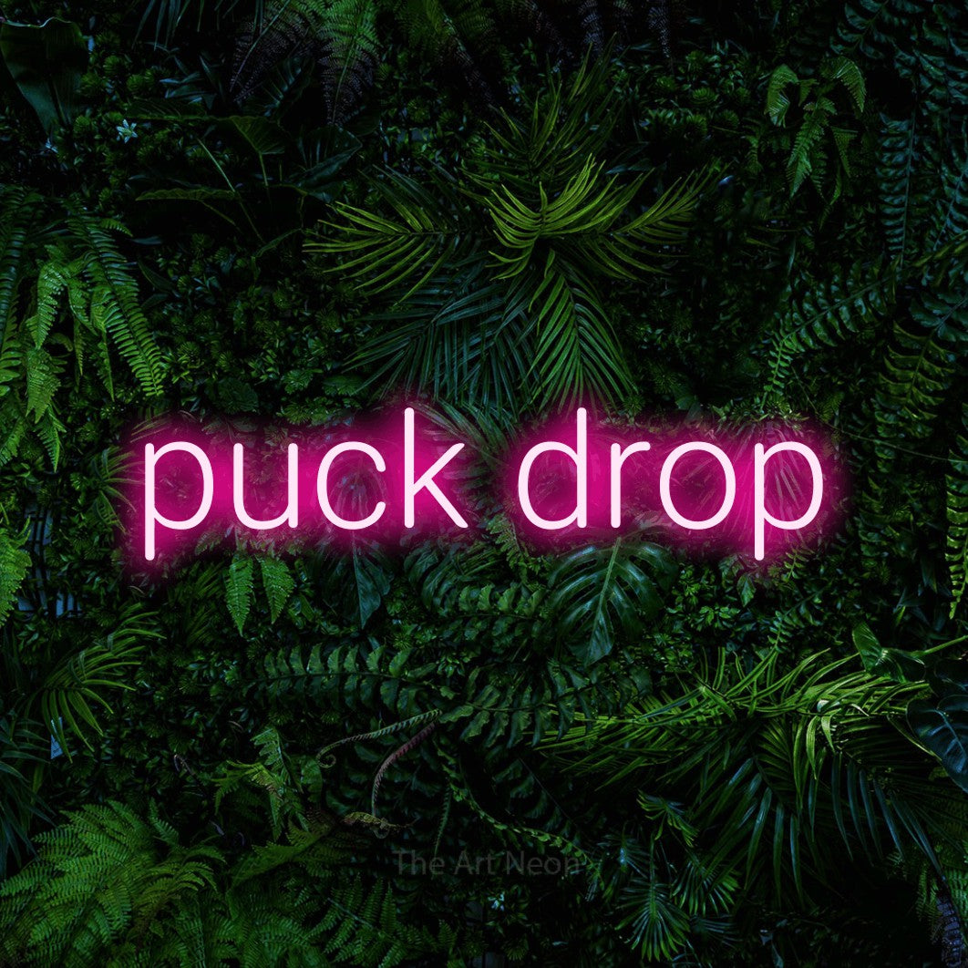 Hot pink LED neon sign reading "Puck Drop" against a dense tropical foliage wall