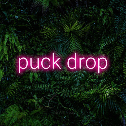 Enseigne néon à DEL à lumière rose vif, affichant « Puck Drop » sur un mur de feuillage tropical dense