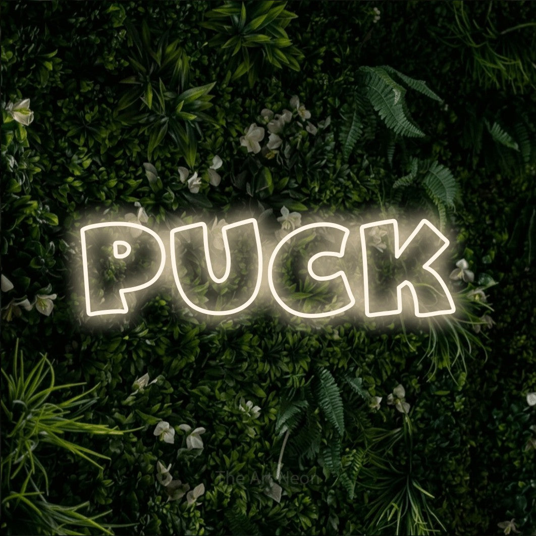 Warm white outline-style LED neon sign reading "Puck" against a leafy green wall
